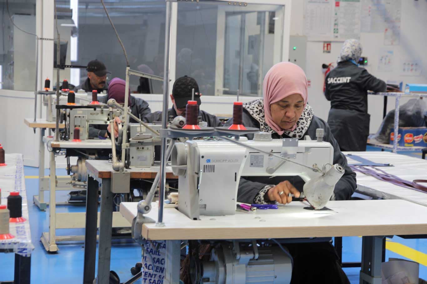 Artisans stitching leather goods on industrial machines at Saccent in Fes, Morocco